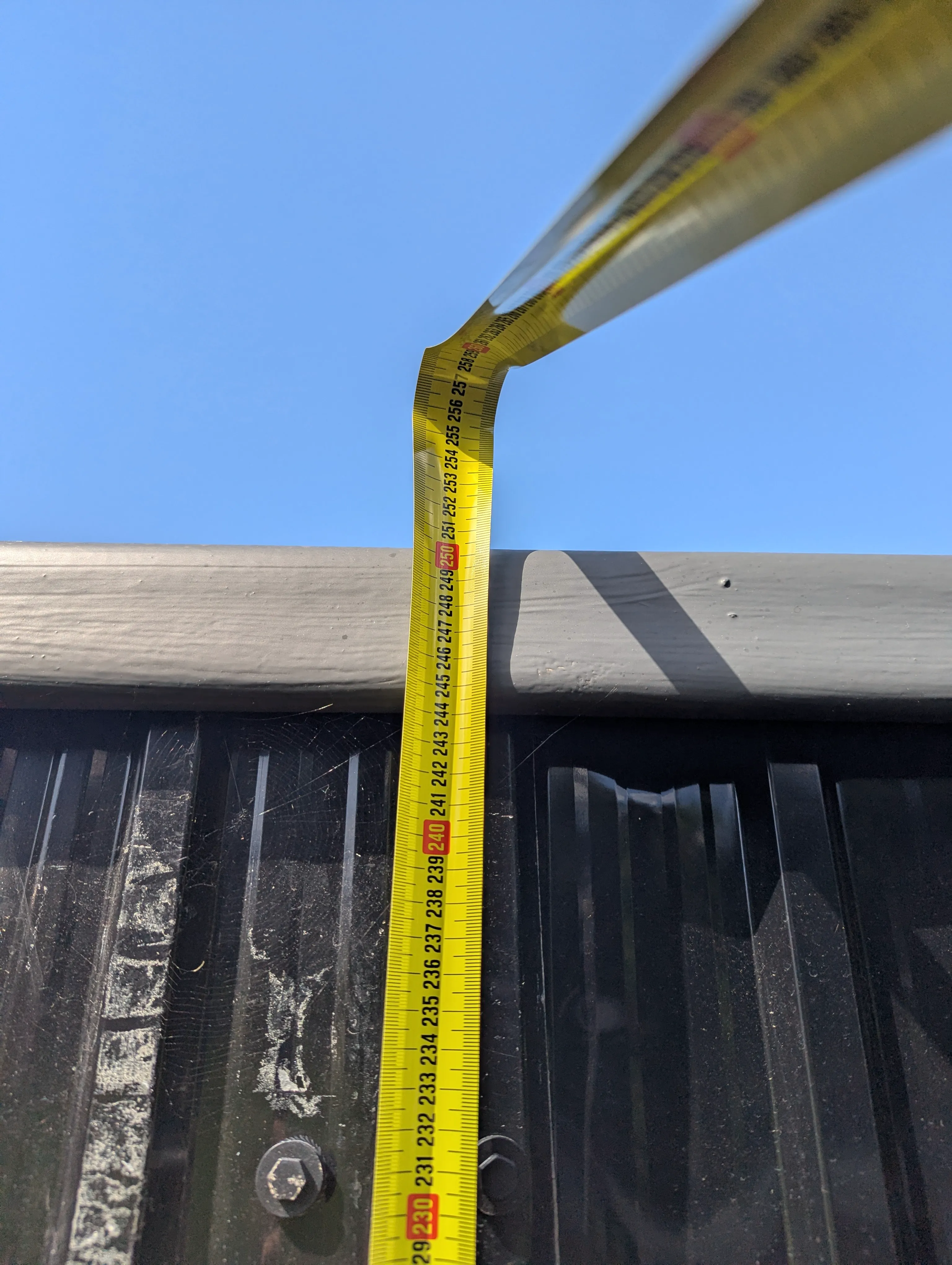 Tape measure run up the outside of the building to the top of the roof coping, reading under 2500mm